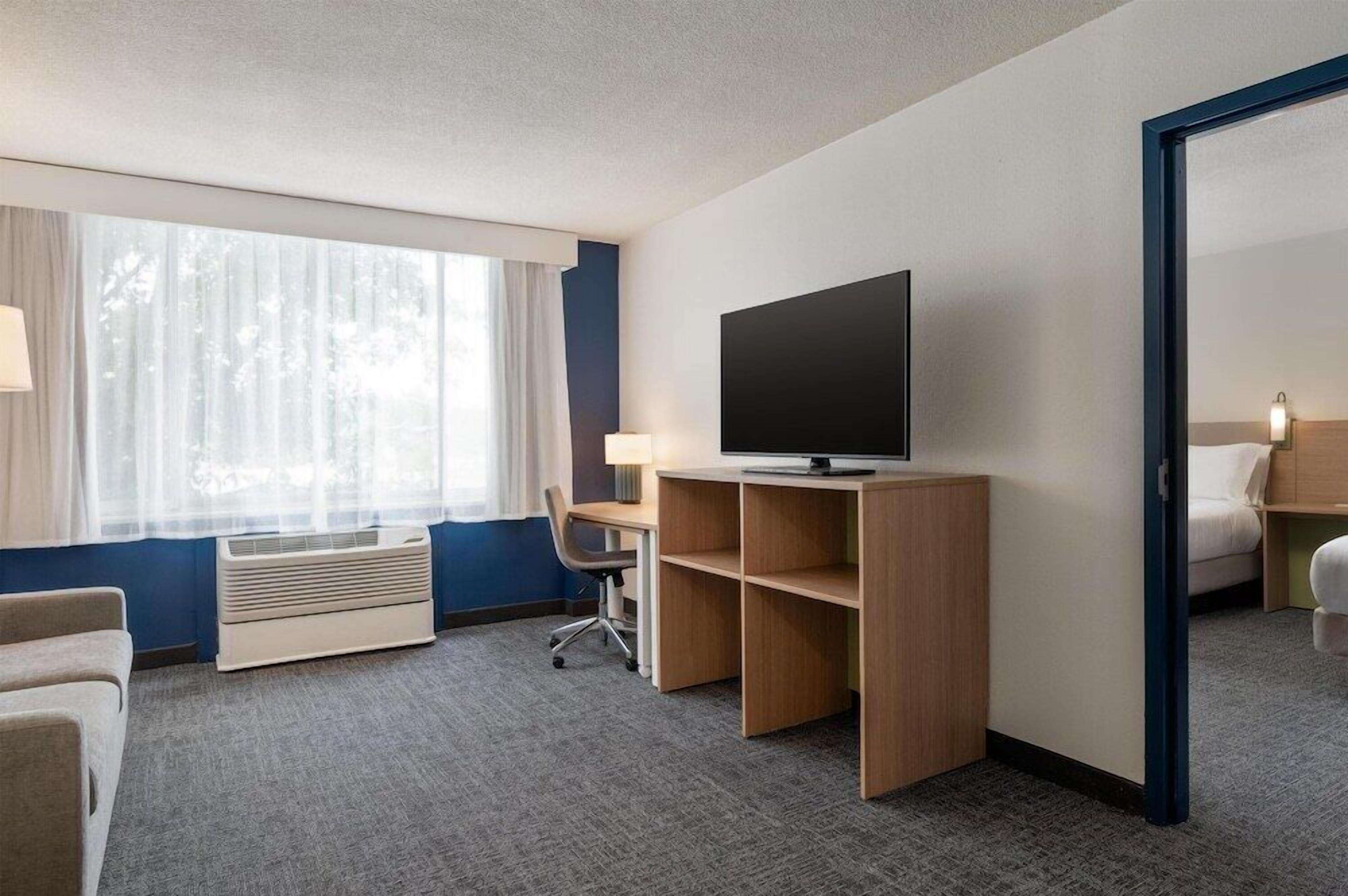 Et hotelværelse med et stort vindue, et fladskærms-tv, et skrivebord med en stol og en seng.