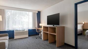 Et hotelværelse med et stort vindue, et fladskærms-tv, et skrivebord med en stol og en seng.
