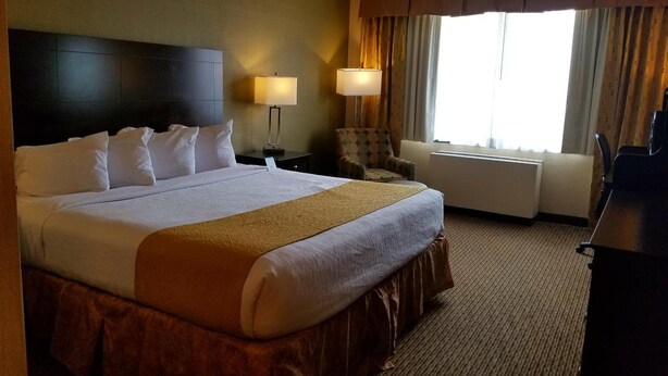 A hotel room with a large bed, a chair, a desk, and a window with curtains.