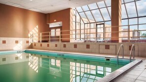 Piscina interior com paredes de vidro transparente, chão revestido e ambiente iluminado pelo sol.