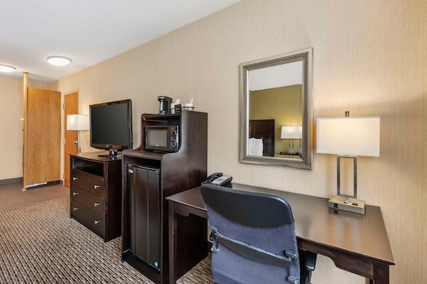 Una habitación de hotel con escritorio, televisión, microondas, teléfono, espejo y lámpara.