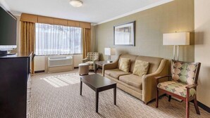 A hotel room with a sofa, armchair, small table, and a television.