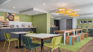 A modern kitchen with a dining area, green walls, and yellow pendant lights.