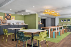 A modern kitchen with a dining area, green walls, and yellow pendant lights.