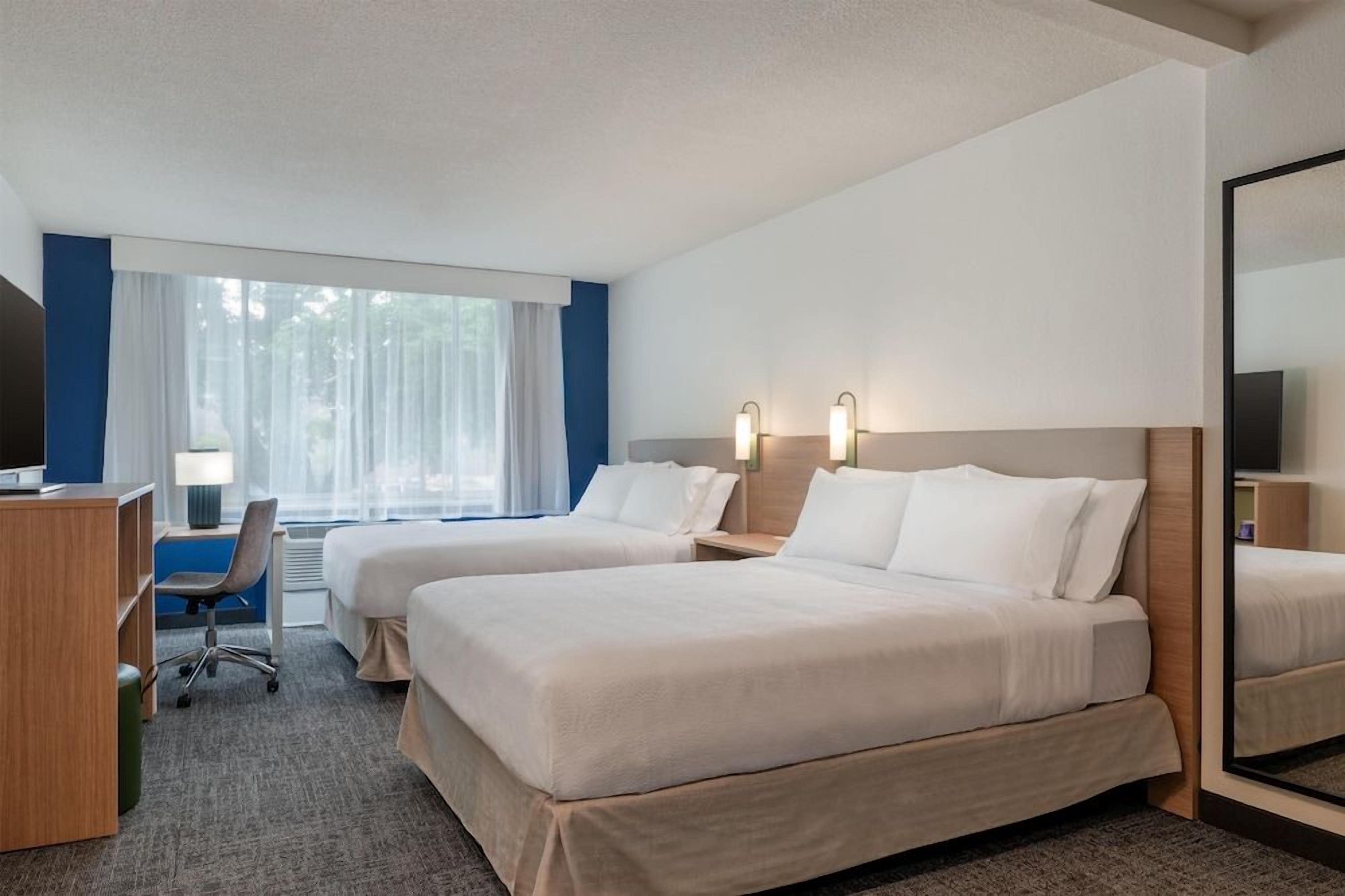 Una habitación de hotel con dos camas, un escritorio, una silla y un espejo grande.