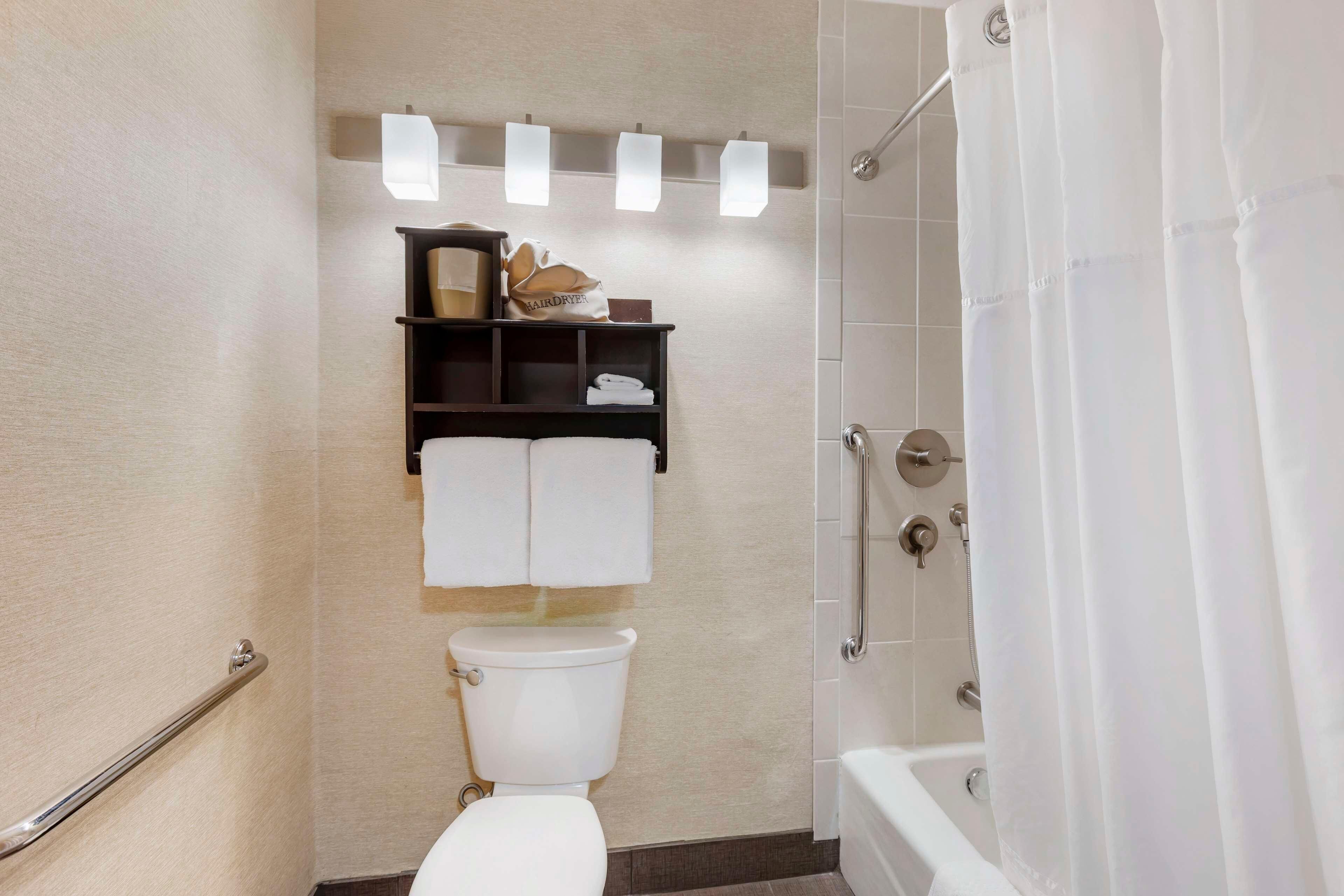 A bathroom with a toilet, a shower with a curtain, a towel rack, and a shelf with toiletries.