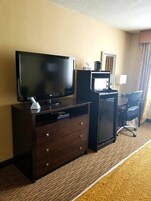 Habitación de hotel con televisión de pantalla plana, un escritorio pequeño con computadora, una silla y una lámpara.