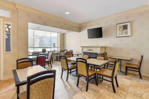 A hotel dining area with multiple tables and chairs, a flat-screen TV mounted on the wall, and a fireplace. - Best Western Watertown Fort Drum (Watertown)