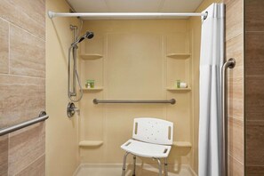 A wheelchair-accessible shower stall with grab bars, a showerhead, and a white chair.
