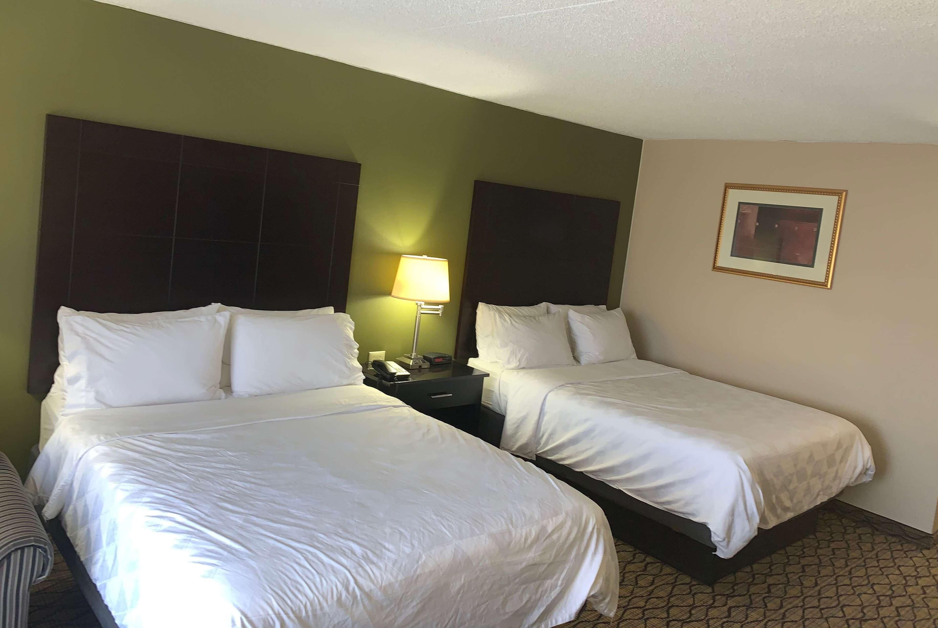 A hotel room with two beds, a nightstand, a lamp, and a framed picture on the wall.