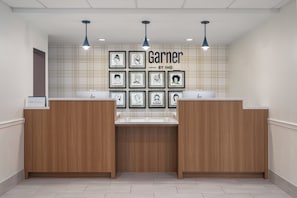A reception area with wooden reception desks, a check-in counter, and framed artwork on the wall. - Garner Hotel Totowa by IHG (Totowa)