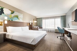 A hotel room with a bed, desk, chair, and a large window with curtains.