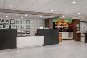 A hotel lobby with a reception desk, framed artwork on the wall, a snack bar, and a 'Pay at Desk' sign. - Garner Hotel Totowa by IHG (Totowa)