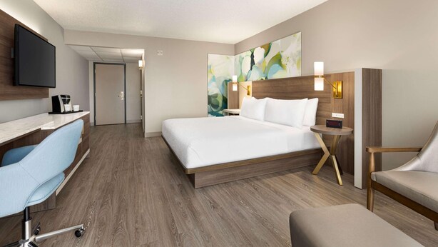 A hotel room with a bed, desk, chair, TV, and artwork on the wall. - Wyndham Garden Totowa (Totowa)