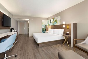 Quarto de hotel com cama, escrivaninha, cadeira, televisão e obras de arte na parede.