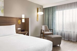 A hotel room with a large bed, a chair, a small table, and a lamp. - Wyndham Garden Totowa (Totowa)