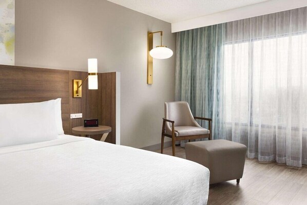 A hotel room with a large bed, a chair, a small table, and a lamp.