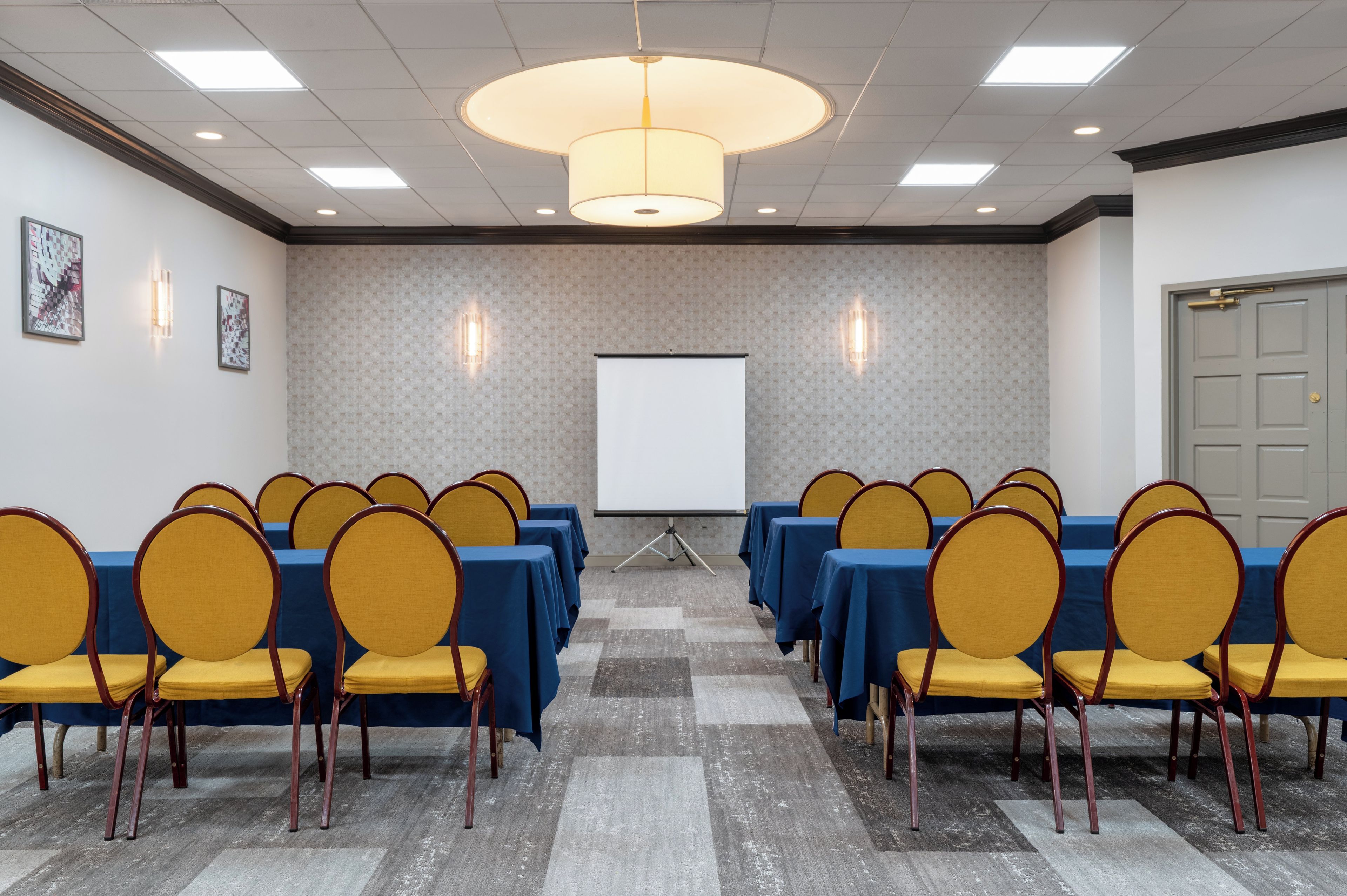 Ein Konferenzraum mit Tischen und Stühlen, einer Projektionsleinwand und einer strukturierten Wand.