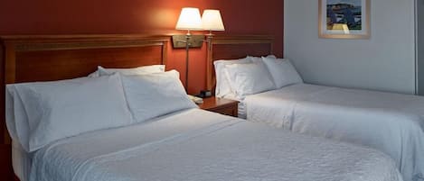A hotel room with two beds, a nightstand with a lamp, and a framed picture on the wall.