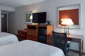 Quarto de hotel com duas camas, uma escrivaninha com computador, televisão, micro-ondas, abajur e espelho.