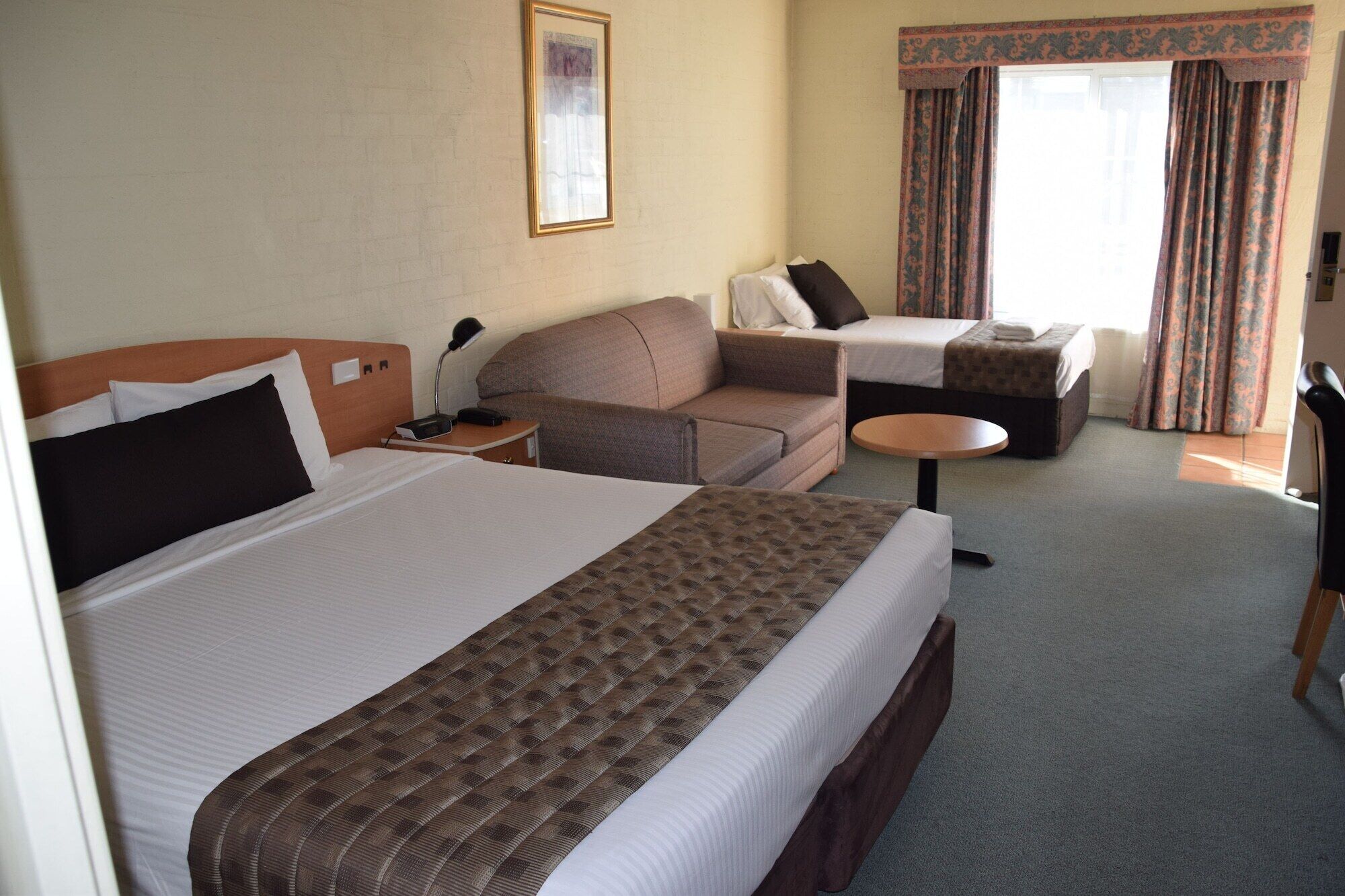 A hotel room with a large bed, a sofa, a small table, and a desk.