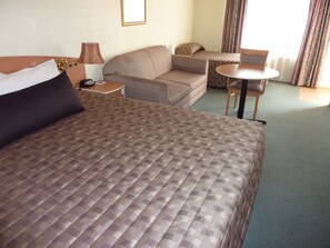 A hotel room with a large bed, a sofa, a small table, and a chair. - Coachmans Inn Motel (Bathurst)