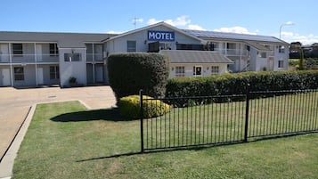 A motel with a sign, a parking lot, and a well-maintained lawn.
