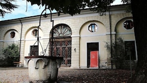 Ein Gebäude mit Rundbogenfenstern, einer großen Steinsäule mit Brunnen und einer roten Tür.
