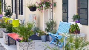Ein Straßencafé mit Außenbestuhlung, einem grünen Sonnenschirm und Blumentöpfen.