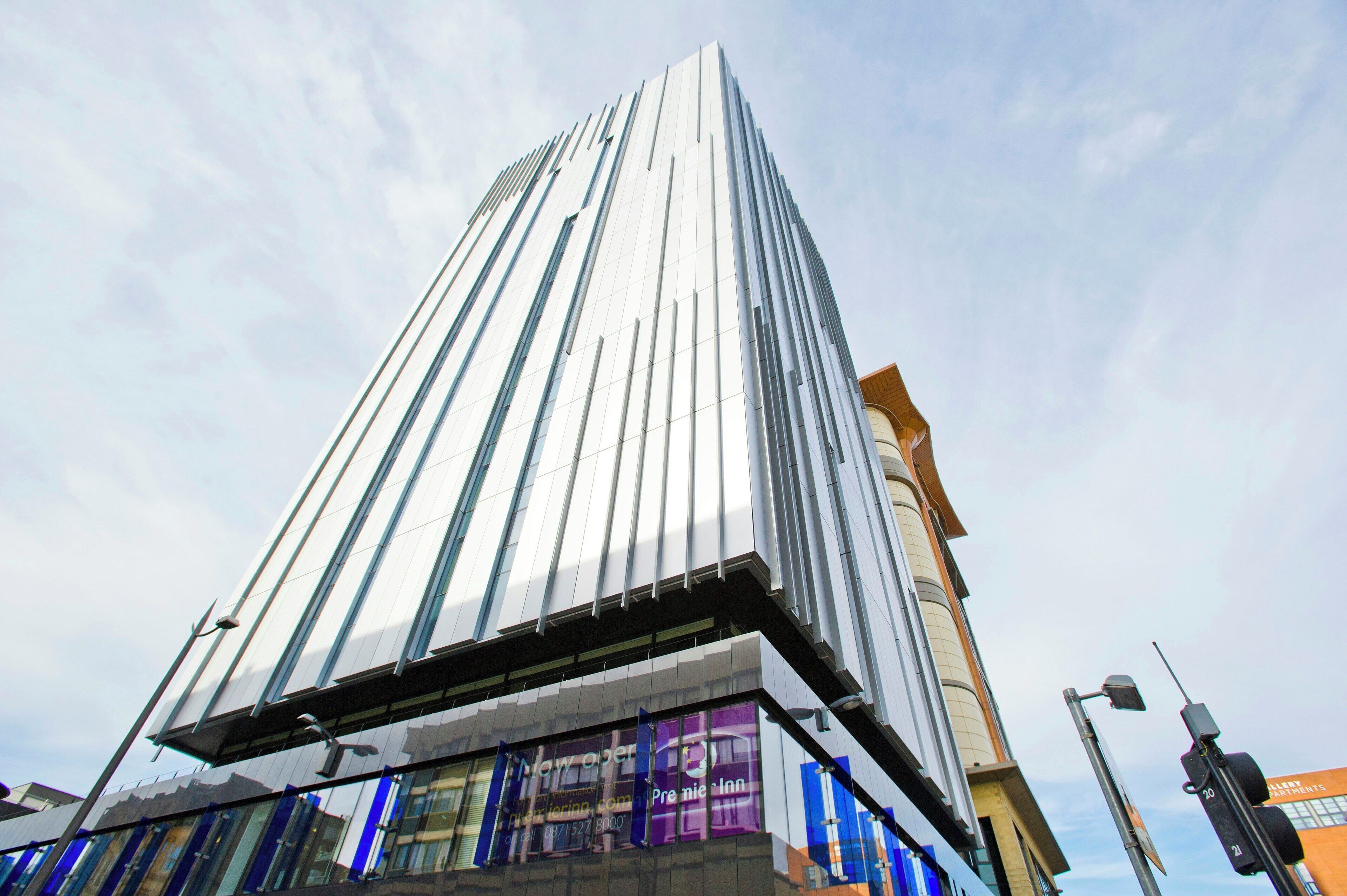 Un edificio moderno de gran altura con fachada de vidrio reflectante, diseño vertical llamativo y entrada visible con señalización.