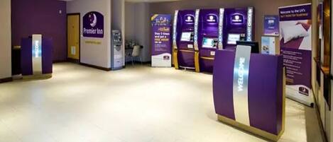 A hotel reception area with a Premier Inn sign, self-service kiosks, and a reception desk.