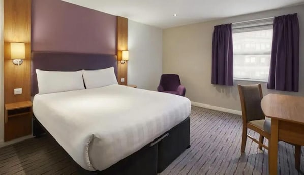 Une chambre d’hôtel avec un grand lit, une chaise, une table et une fenêtre avec des rideaux.