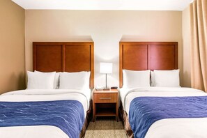 A hotel room with two beds, a nightstand, a lamp, and a window with curtains.