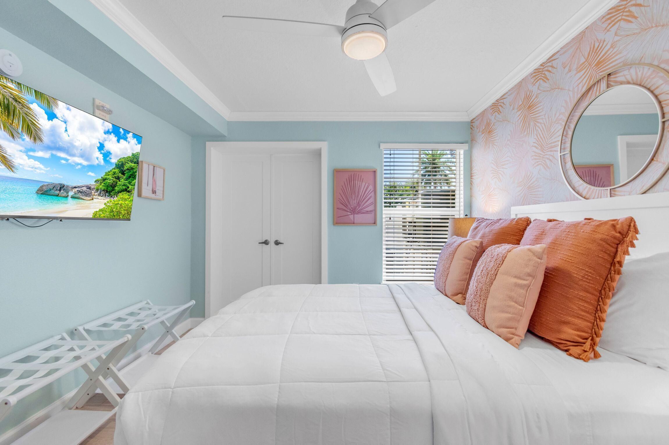 Un dormitorio con cama, ventilador de techo, televisor, puerta y ventana con persianas.