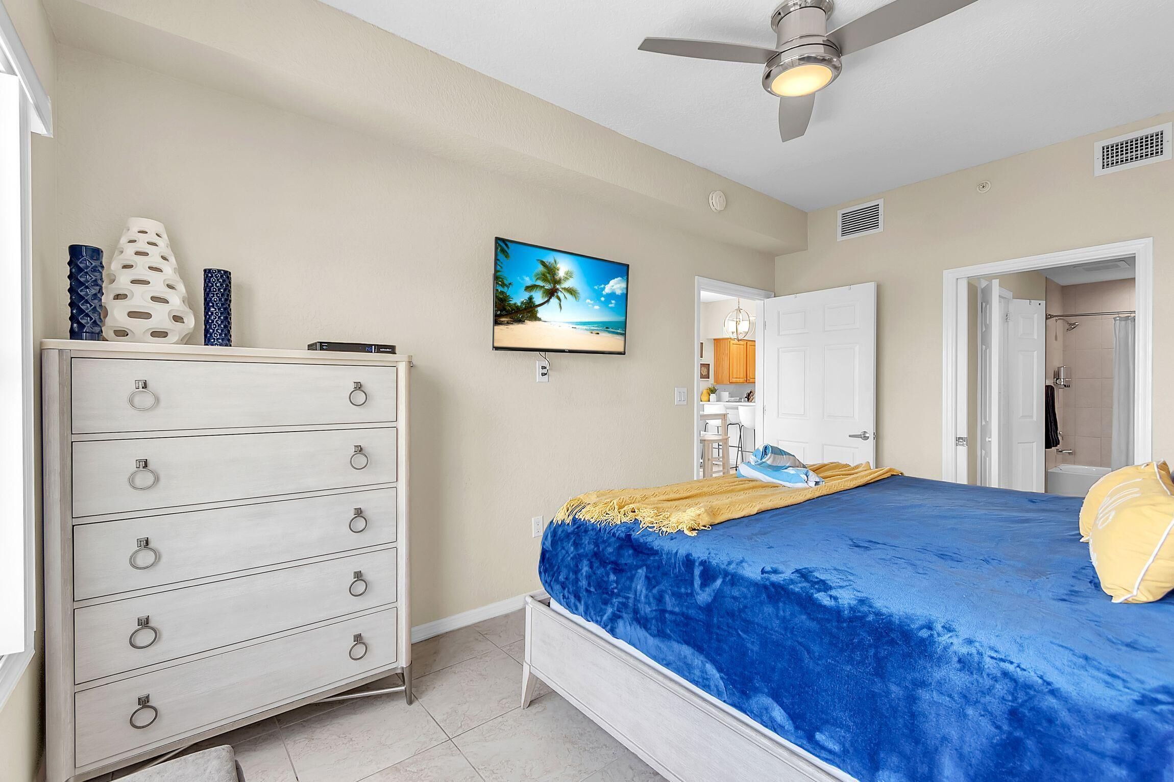Een slaapkamer met een bed, een dressoir, een televisie en een deur naar een badkamer.