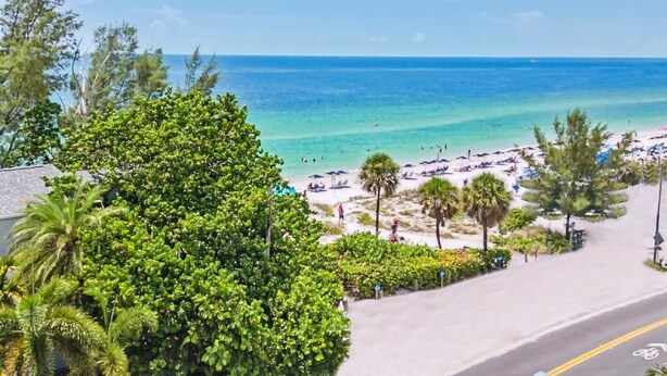 A coastal road with a beach view, including a paved path, beach umbrellas, and palm trees. - Sunset Beach House (Treasure Island)