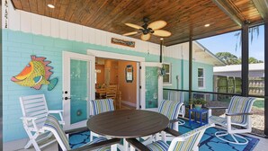 A covered patio with a round table and striped chairs, a ceiling fan, and a fish mural on the wall. - Sunny Dayz (New Smyrna Beach)