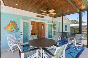 A covered patio with a round table and striped chairs, a ceiling fan, and a fish mural on the wall. - Sunny Dayz (New Smyrna Beach)