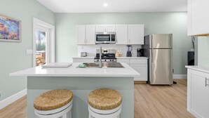 A modern kitchen with white cabinets, stainless steel appliances, and a central island with two stools. - Lofty House (New Smyrna Beach)