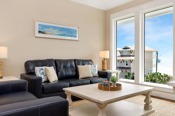 A living room with a black leather sofa, a white coffee table, and a large window with a view of buildings. - Sand Pearl (Port St. Joe)