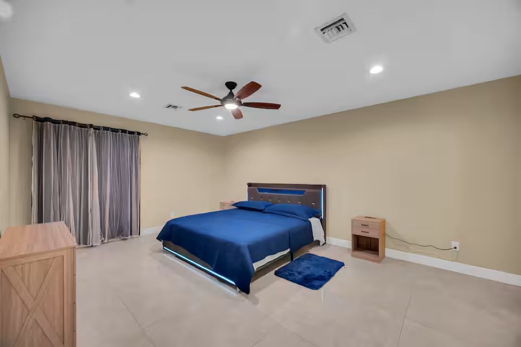Une chambre à coucher avec un lit, un ventilateur de plafond, une table de chevet et un bureau.