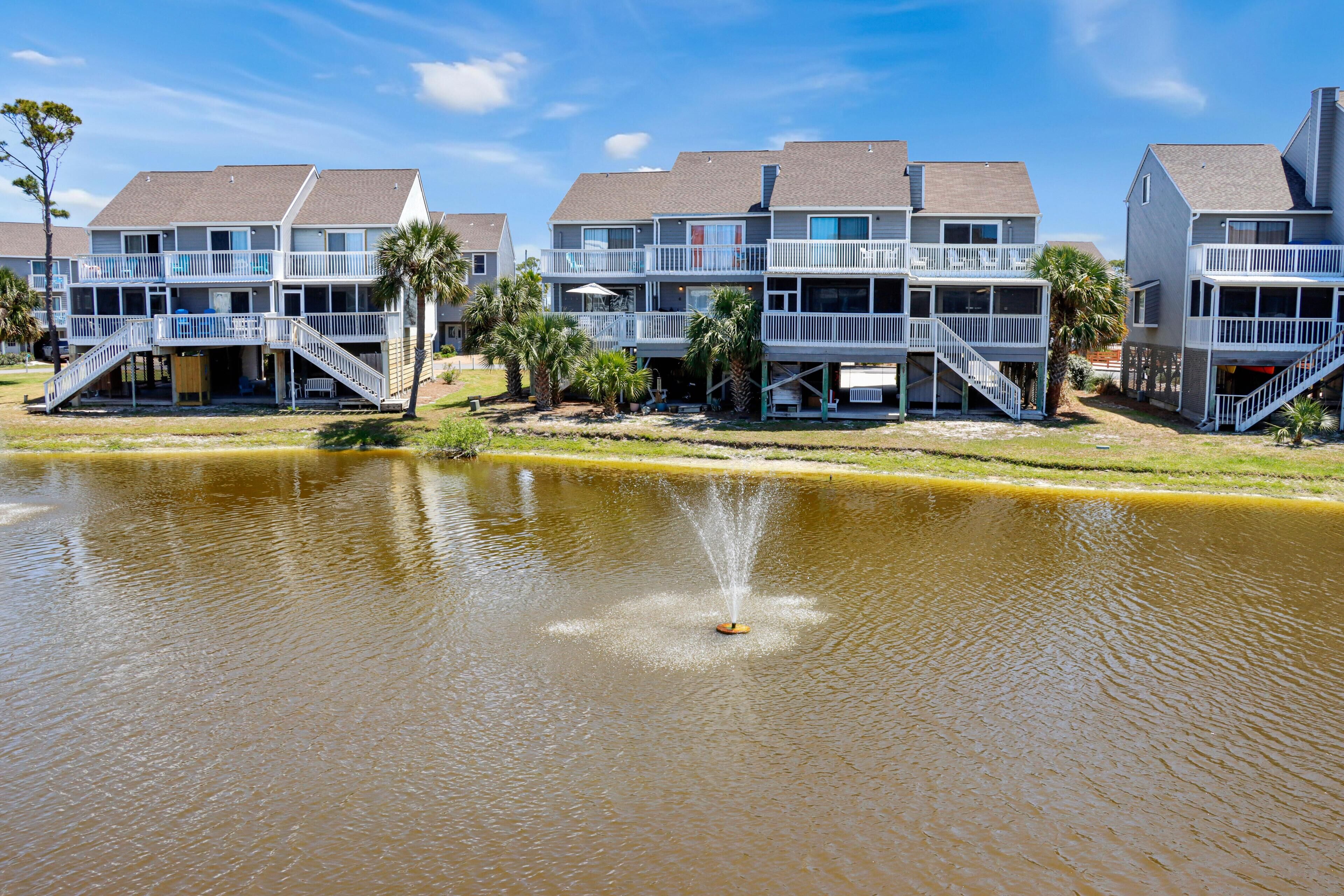 A waterfront hotel with multiple balconies, a central water feature, and a grassy area.