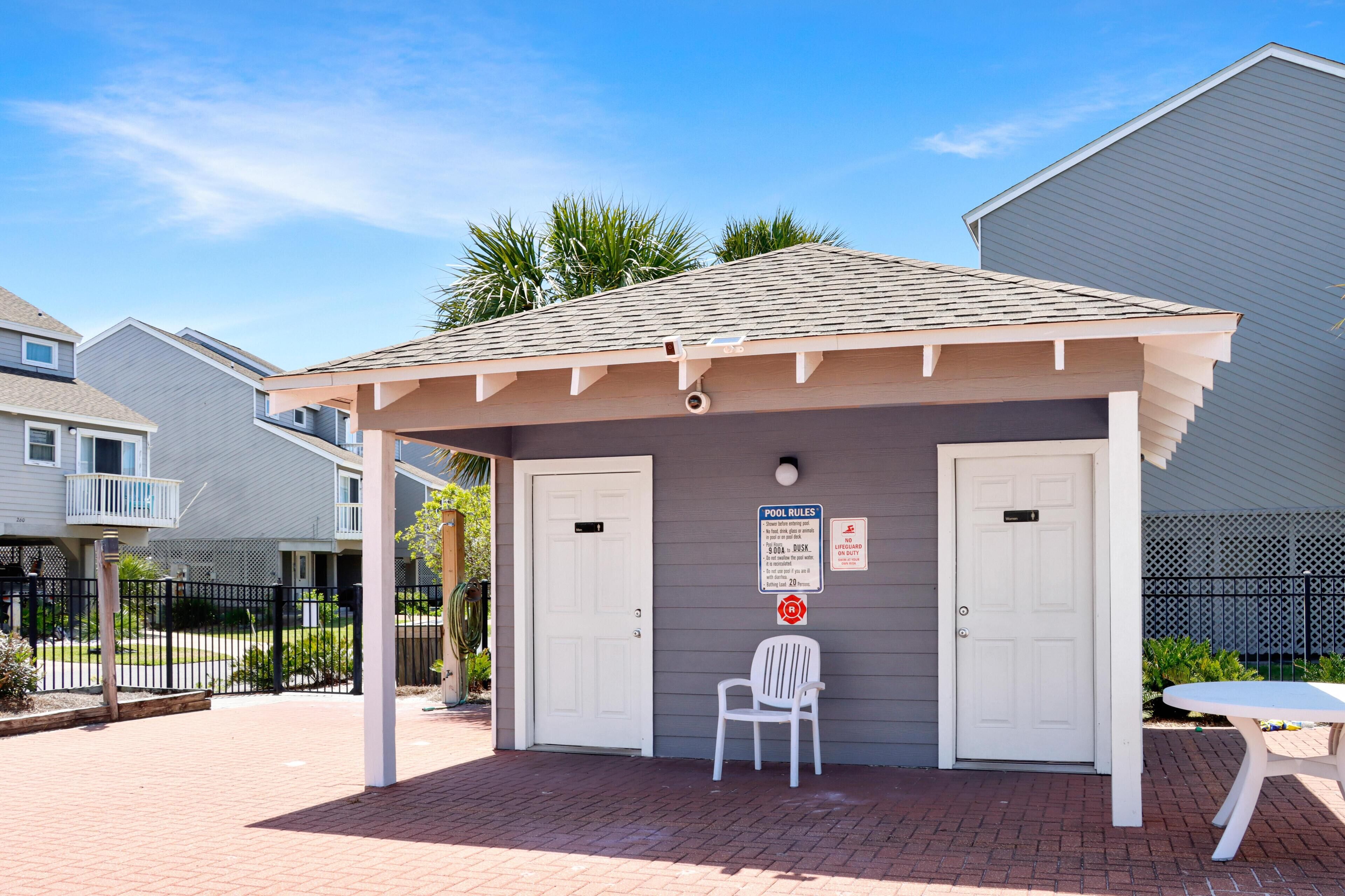 A covered outdoor seating area with a white chair, a table, and a pool rules sign.