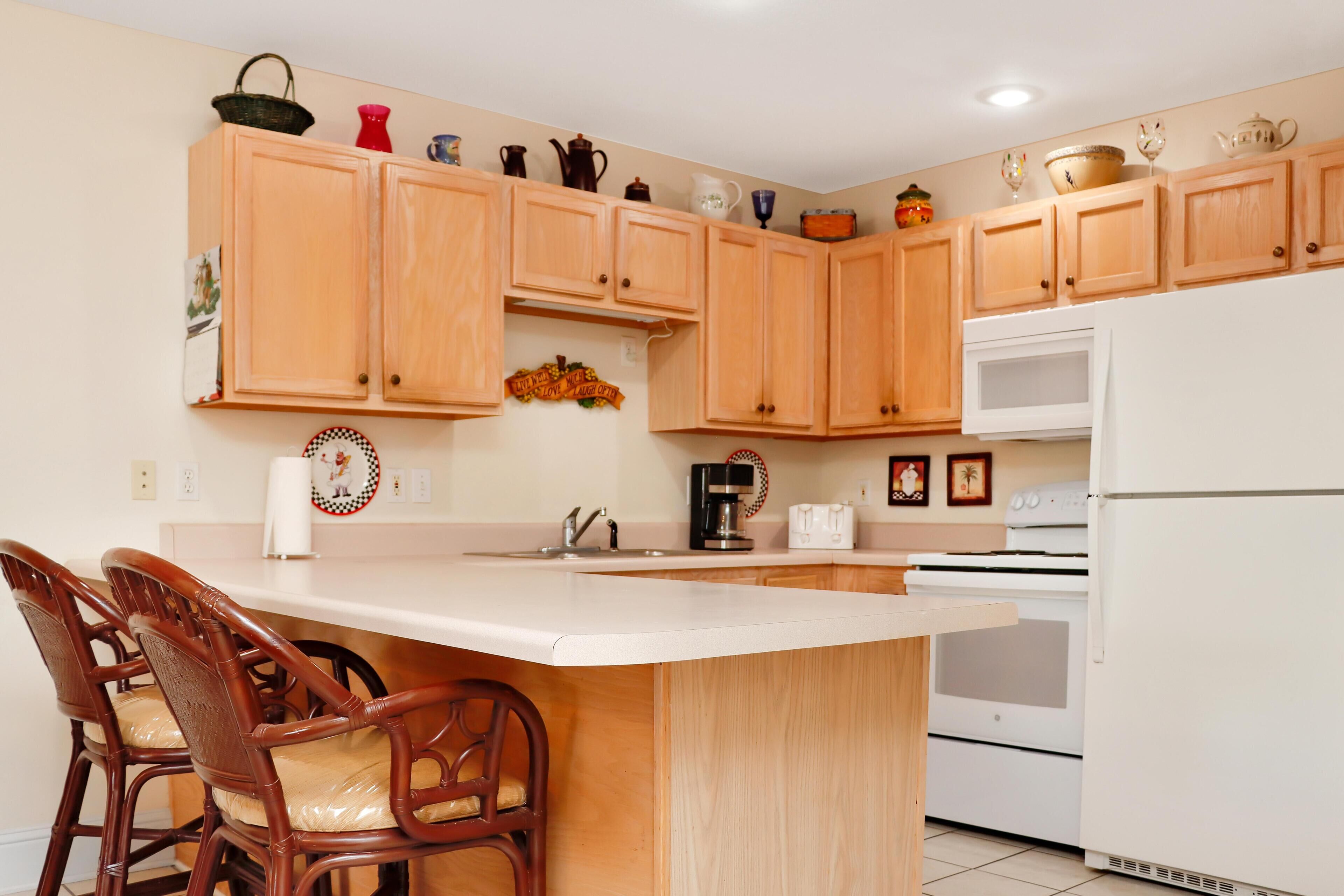 A kitchen with wooden cabinets, a white refrigerator, a stove, and two bar stools.