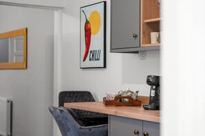 Una kitchenette con una cafetera, un hervidor de agua y un cuadro con un dibujo de chile.