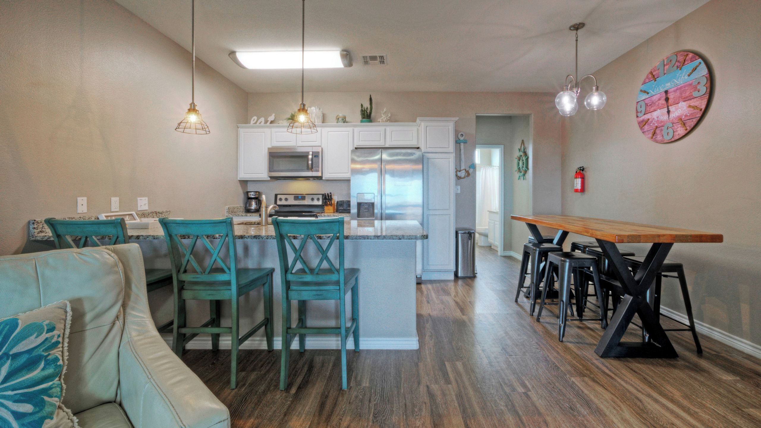 Une cuisine moderne avec des meubles blancs, un îlot central et un coin repas comprenant une table et des chaises en bois.