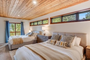 A bedroom with two beds, wooden ceiling, large windows, and a balcony.