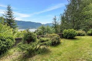 Ein üppiger Garten mit einer Steinmauer, dichter Bepflanzung und Blick auf einen See und Berge.
