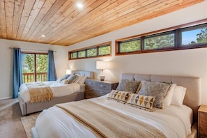 A bedroom with two beds, wooden ceiling, large windows, and a balcony.