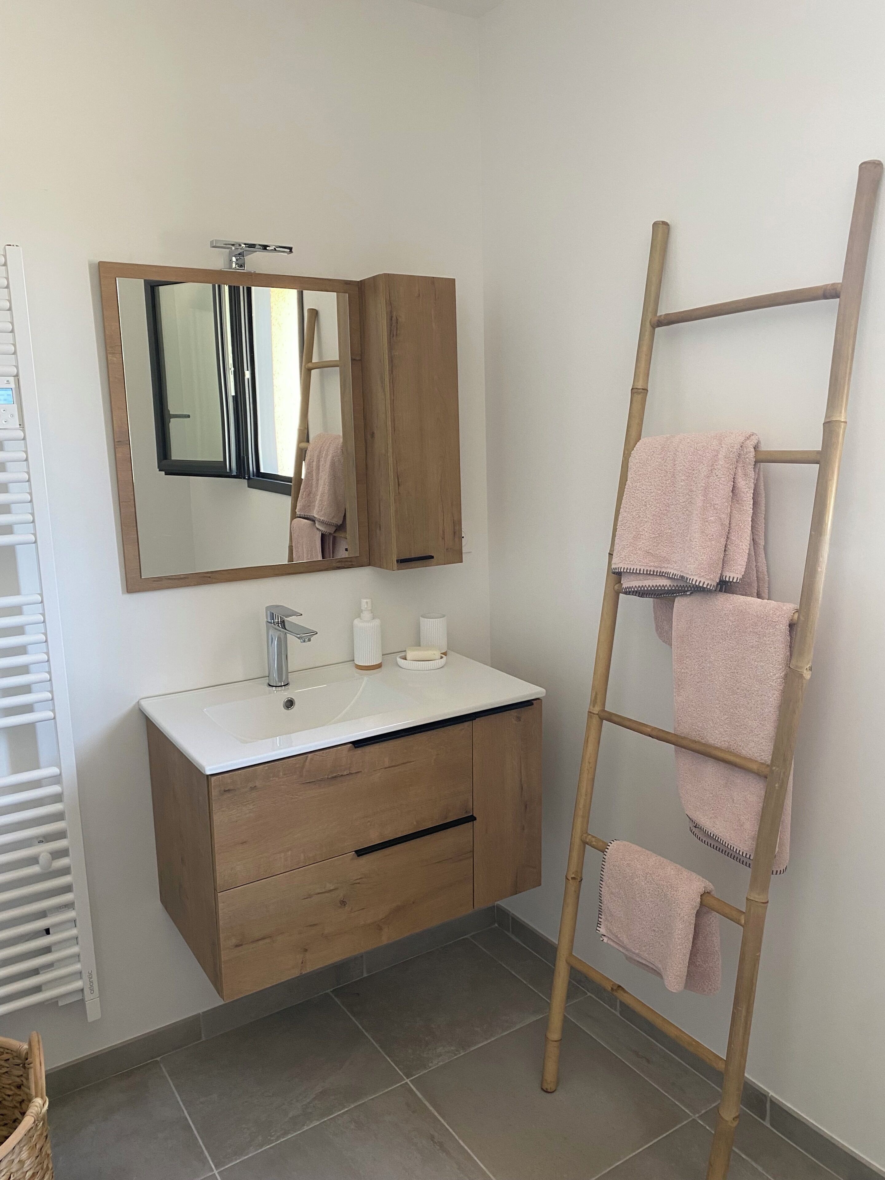 Un baño con tocador de madera, un espejo, un lavabo blanco y un perchero con toallas.